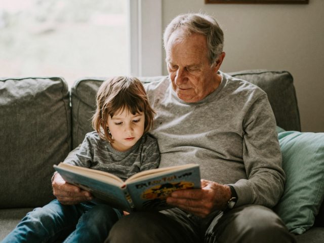Großvater liest Enkelkind gemeinsam auf dem Sofa aus einem Bilderbuch vor